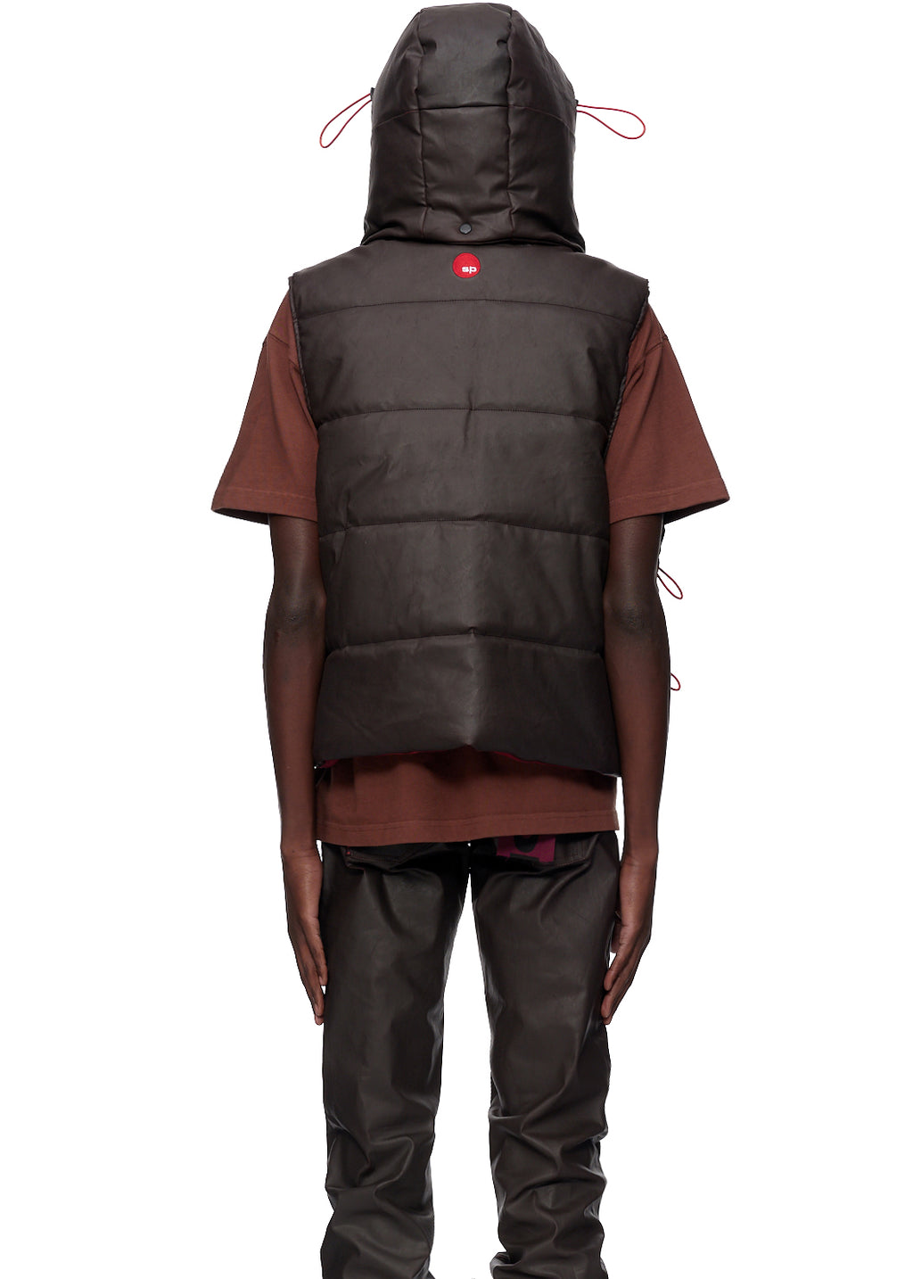 Brown coated canvas hooded puffer vest with red SP5DER logo, worn over a brown t-shirt.