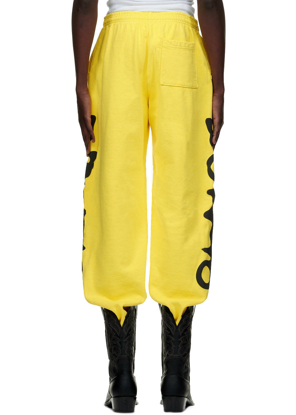 Yellow BELUGA SWEATPANT with black 'Worldwide' puff/discharge print down both legs, worn with black cowboy boots.