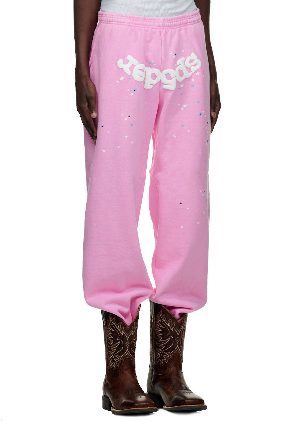 Pink fleece sweatpants with "Sp5der" puff print and star details, worn with cowboy boots.