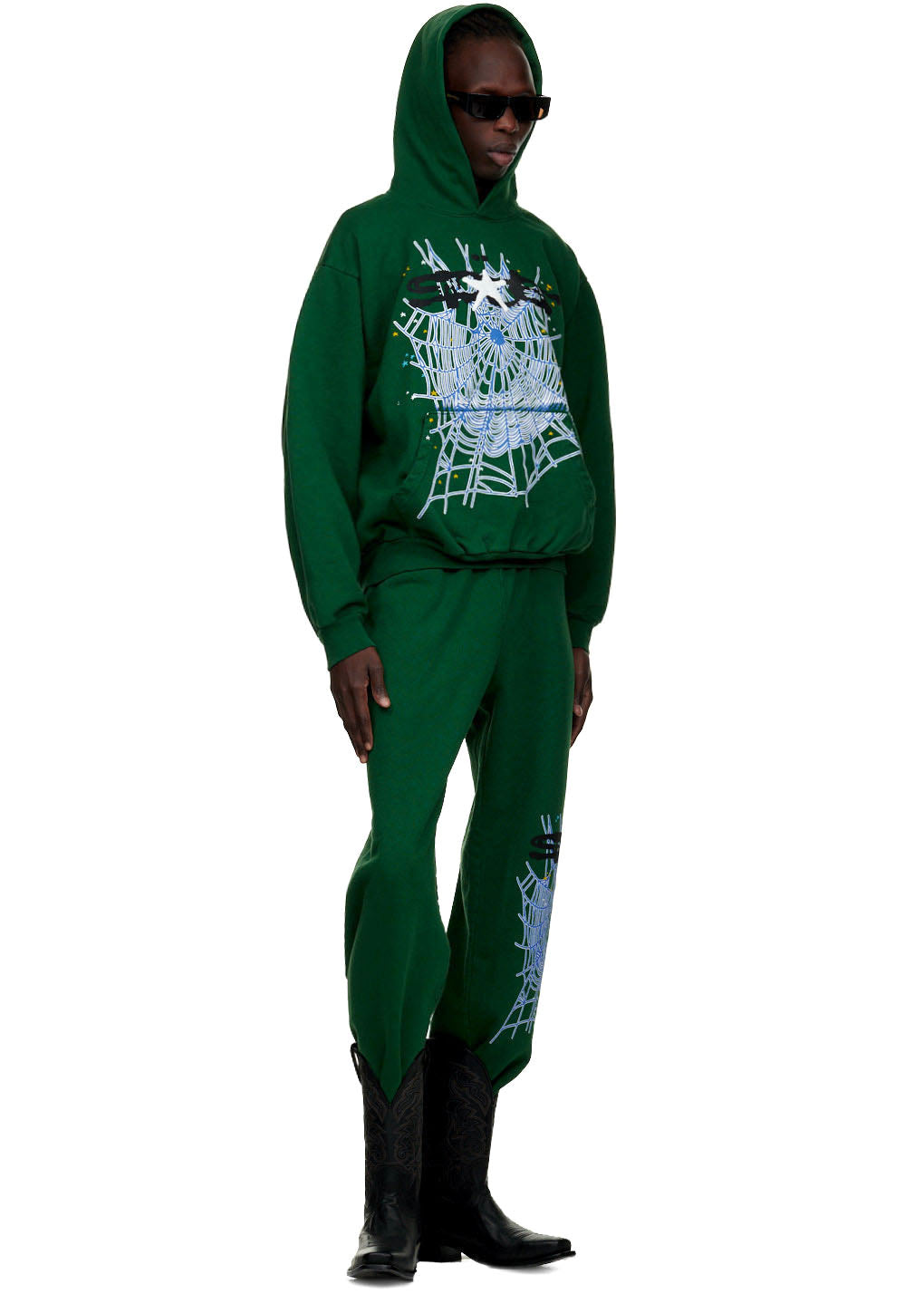 Male model in green WEB SWEATPANT and matching hoodie with SP5DER text and web print.
