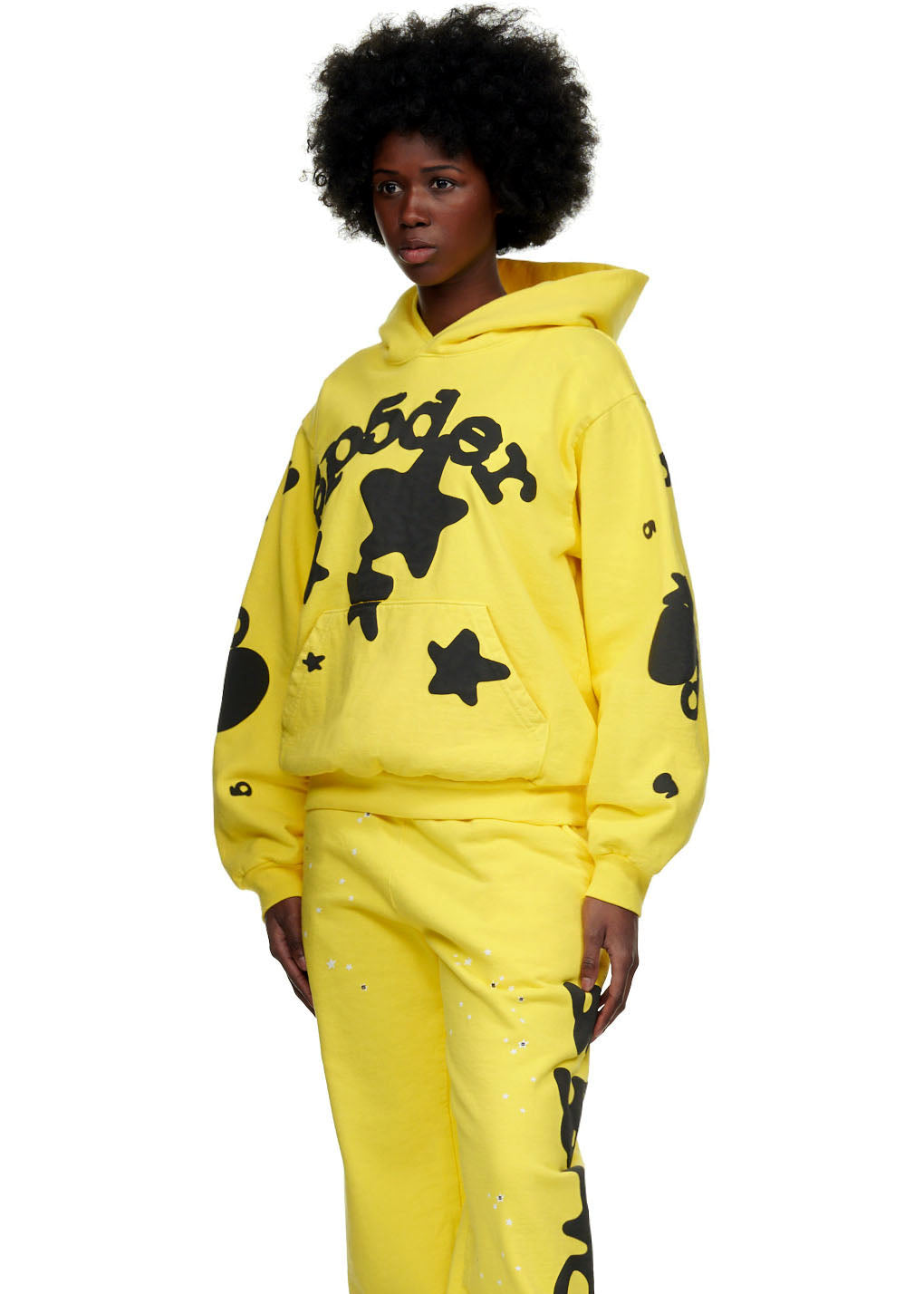 Female model in yellow Beluga Hoodie with black 'SP5DER' and star print, matching sweatpants.